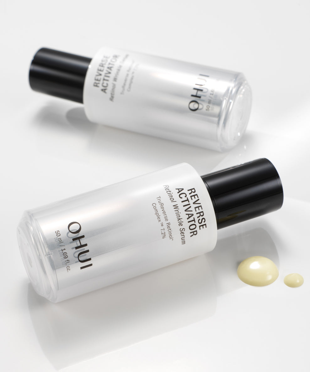 Two bottles of Reverse Activator Retinol Wrinkle Serum laying opposite directions on a white surface, next to a quarter-sized drop of product.