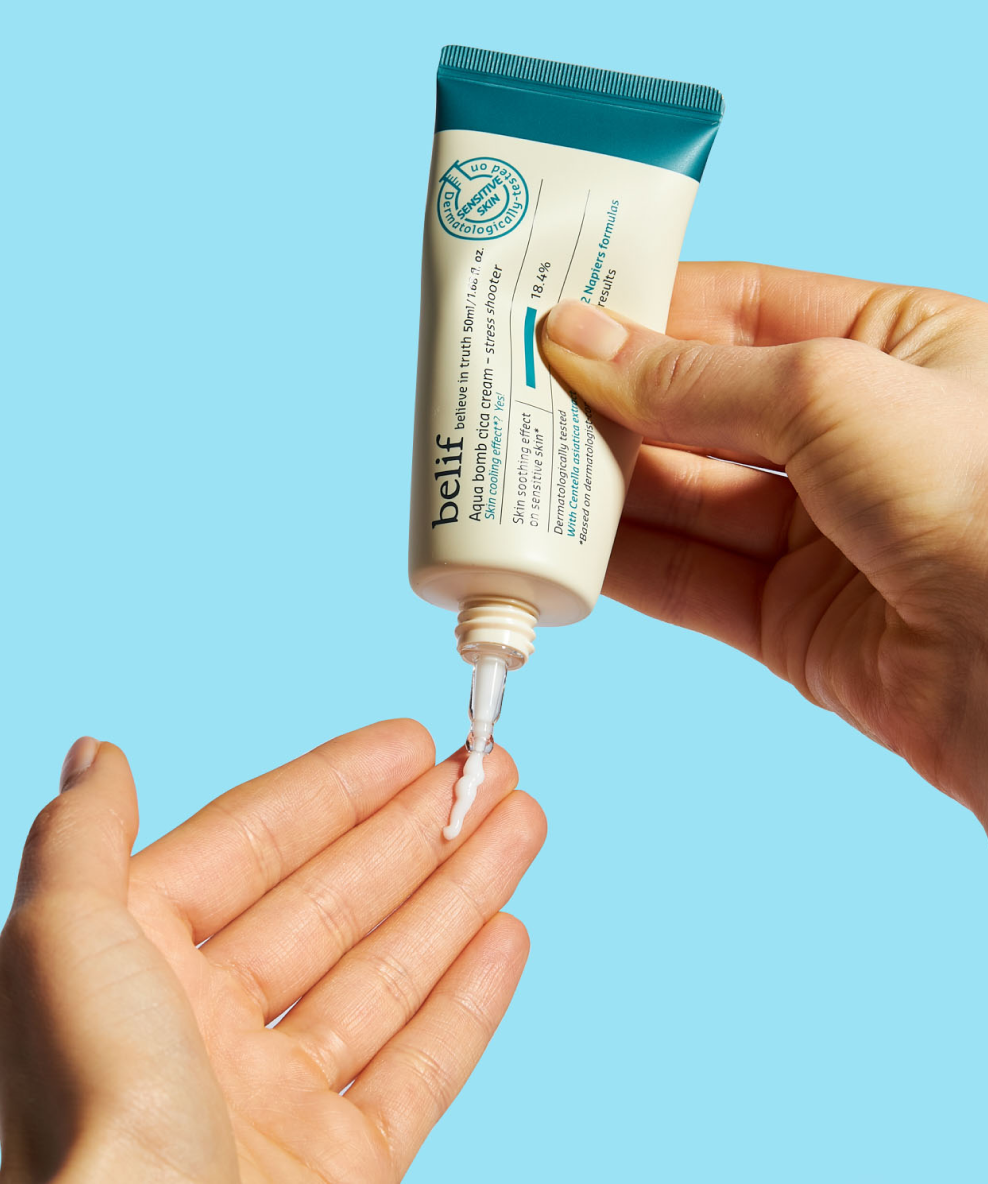 A person uses their right hand to squeeze a tube of belif Aqua Bomb Cica Cream – Stress Shooter 50mL onto their left hand