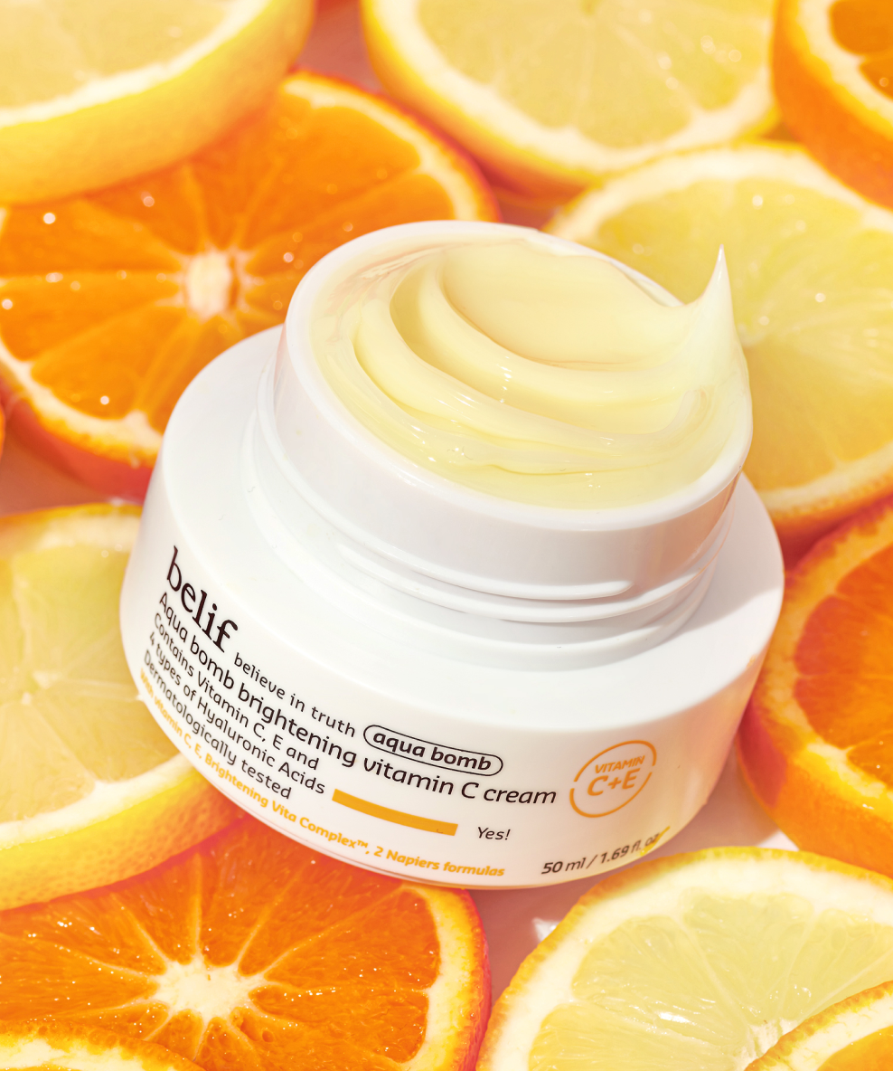 An open jar of belif Aqua Bomb Brightening Vitamin C Cream rests on a base of orange and lemon slices